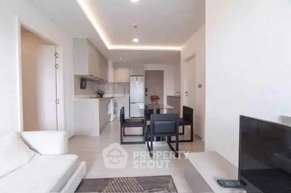 Modern open-plan living room with sleek kitchen and dining area, featuring contemporary furniture and neutral tones.