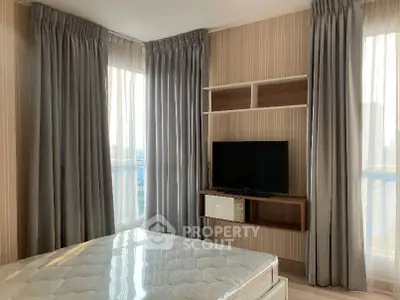 Modern bedroom with large windows and wall-mounted TV, featuring elegant curtains and a comfortable mattress.