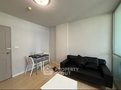 Modern living room with sleek black sofa and minimalist dining area in a cozy apartment.