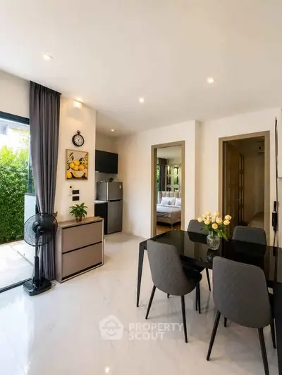 Modern dining area with sleek black table, elegant chairs, and view into a cozy bedroom, perfect for stylish living.