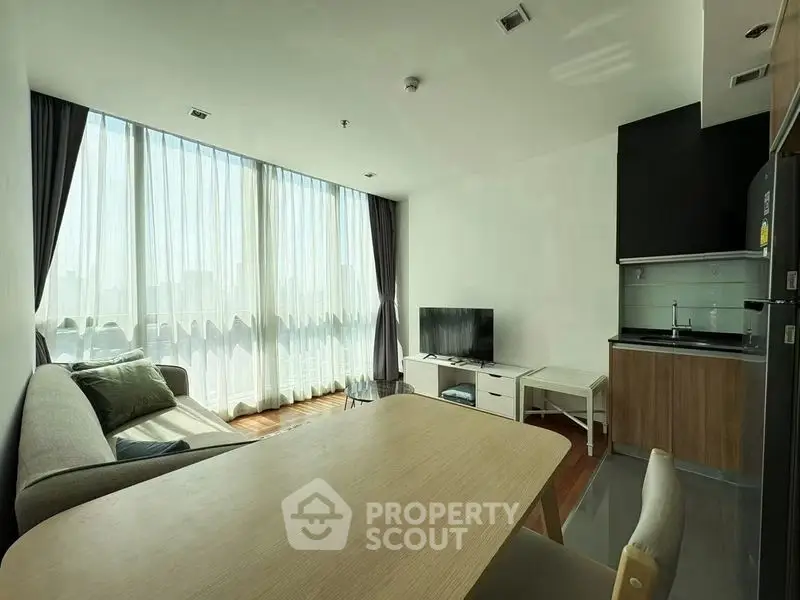 Modern living room with large windows and compact kitchen in open layout apartment.