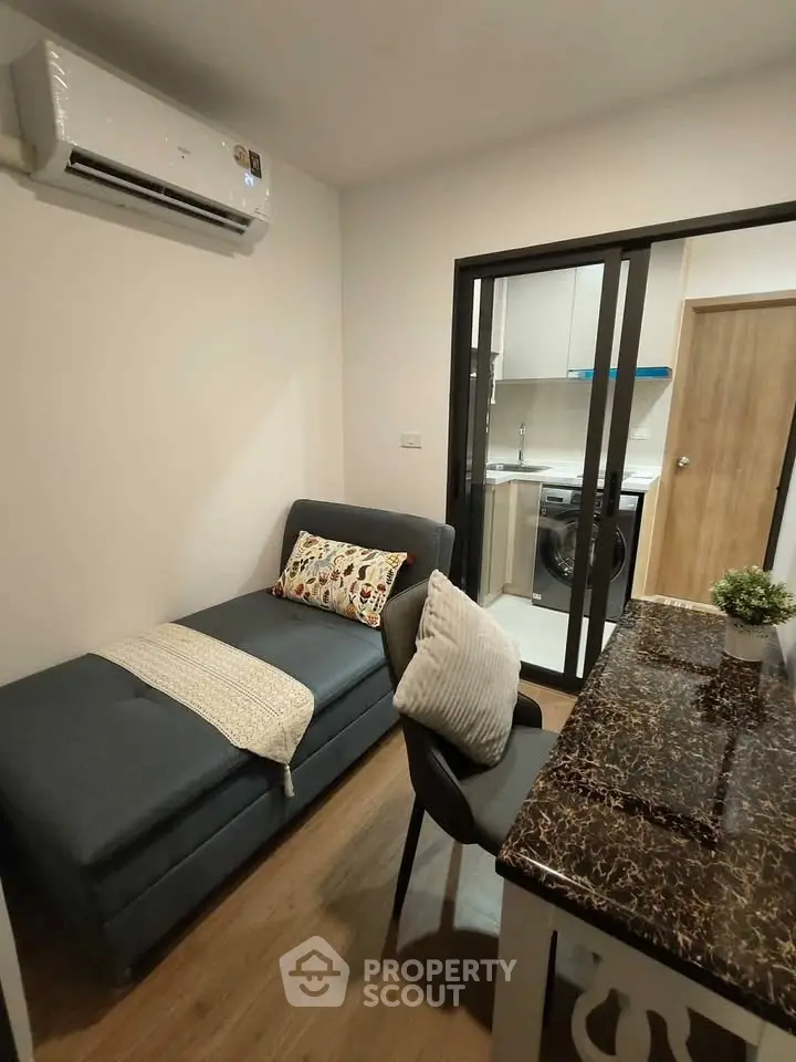 Modern living room with cozy sofa and view into compact kitchen with washing machine.