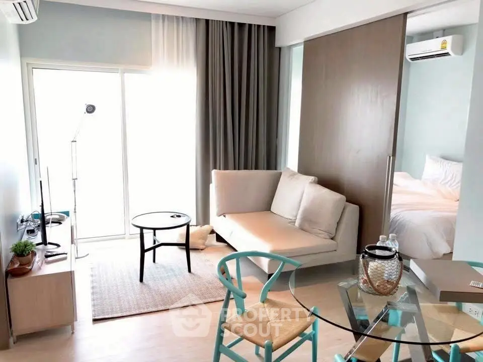 Modern living room with glass dining table and cozy sofa, adjacent to a bright bedroom.