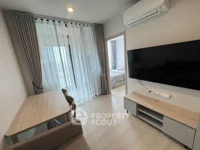 Modern living room with sleek furniture and large TV, adjacent to a cozy bedroom.
