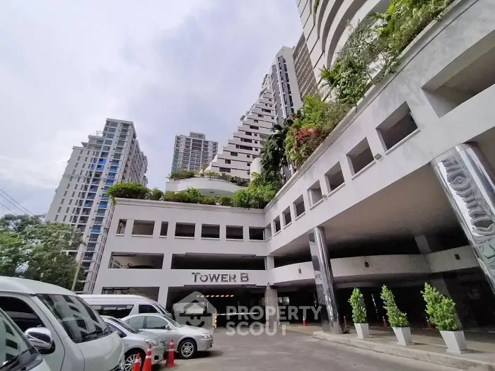 Modern high-rise building with lush greenery and spacious parking area in urban setting.