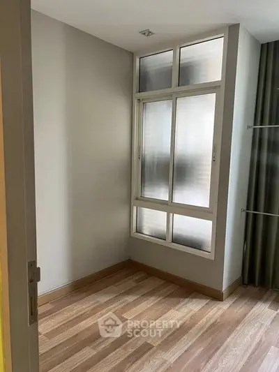 Spacious room with large window and wooden flooring, ideal for customization.