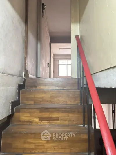 Inviting wooden staircase with contrasting black steps and a vibrant red handrail leading to a bright upper level, enhancing the property's character.