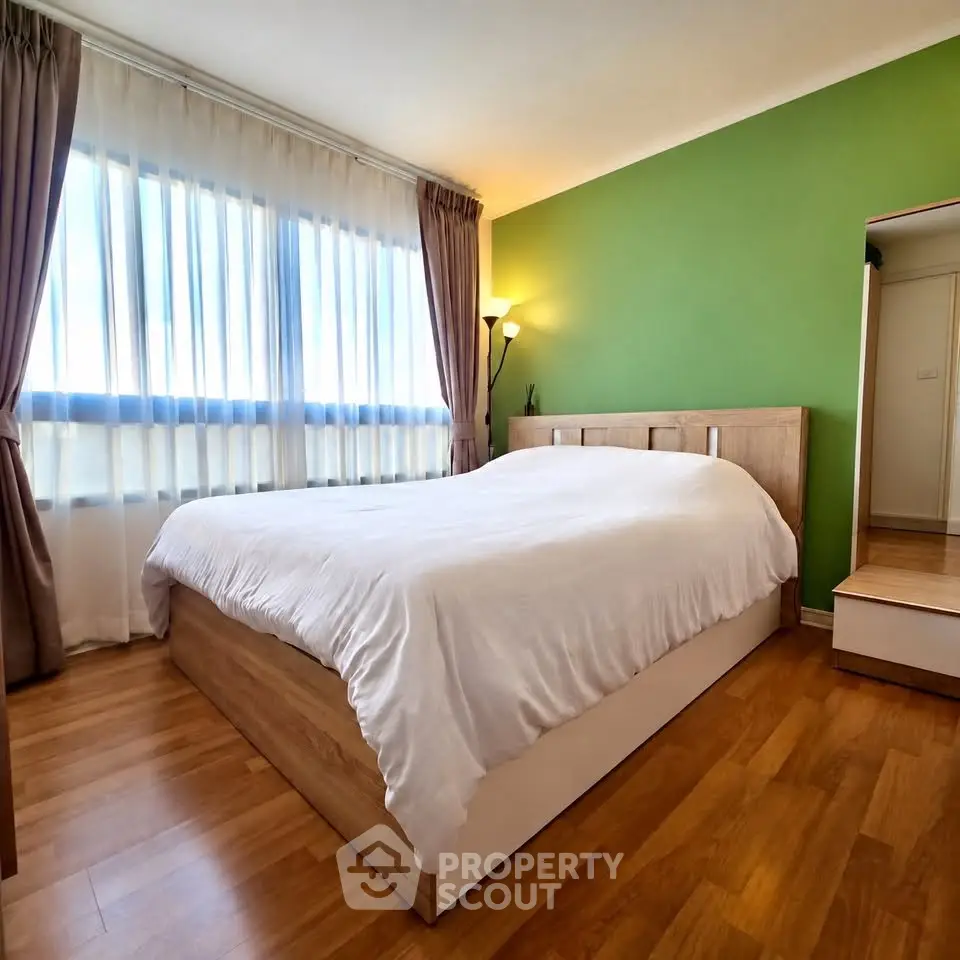 Spacious bedroom with green accent wall and large window for natural light.