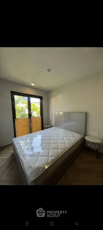 Modern bedroom with large window and natural light, featuring a new mattress and sleek design.