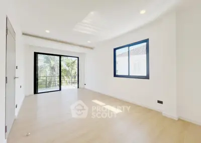 Spacious and bright living room with large windows and balcony access, featuring modern wooden flooring.
