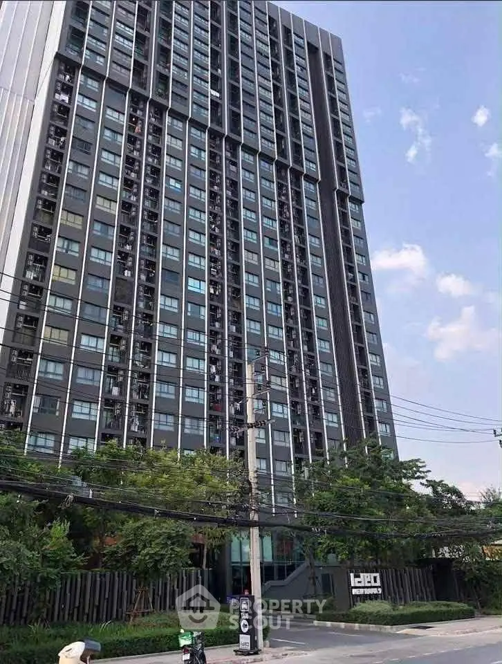 Modern high-rise building with sleek design and lush greenery in urban setting.