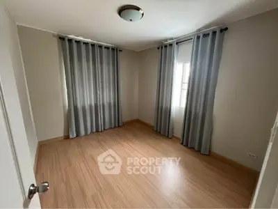 Spacious empty bedroom with wooden flooring and large windows.