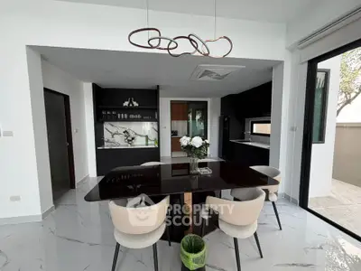 Modern dining area with sleek black table, elegant chairs, and open kitchen layout in a stylish home.