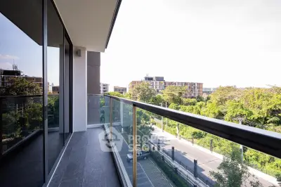 Spacious balcony with glass railing offering a stunning view of lush greenery and modern buildings.