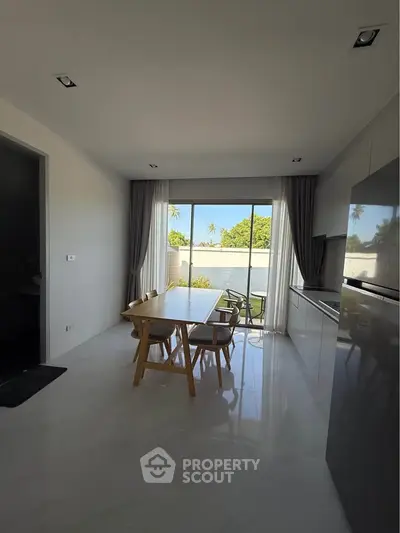 Modern kitchen with open layout and garden view, featuring sleek cabinetry and dining area.