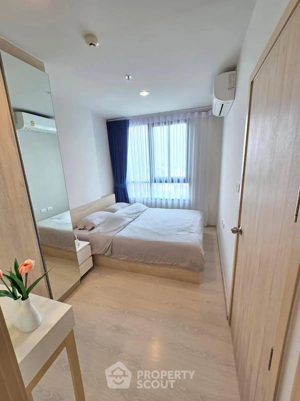 Modern bedroom with minimalist decor, large window, and wooden flooring in a cozy apartment.