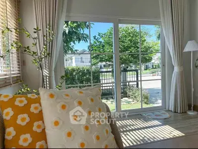 Bright living room with large window overlooking lush garden, featuring cozy floral cushions and elegant curtains.
