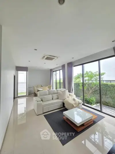 Spacious modern living room with large windows and garden view, featuring elegant furniture and sleek design.
