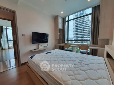 Modern bedroom with large window and city view, featuring a wall-mounted TV and stylish furnishings.