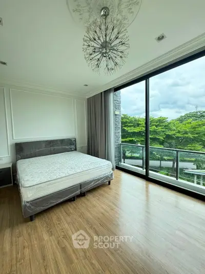 Spacious bedroom with large windows and scenic view, featuring modern chandelier and wooden flooring.