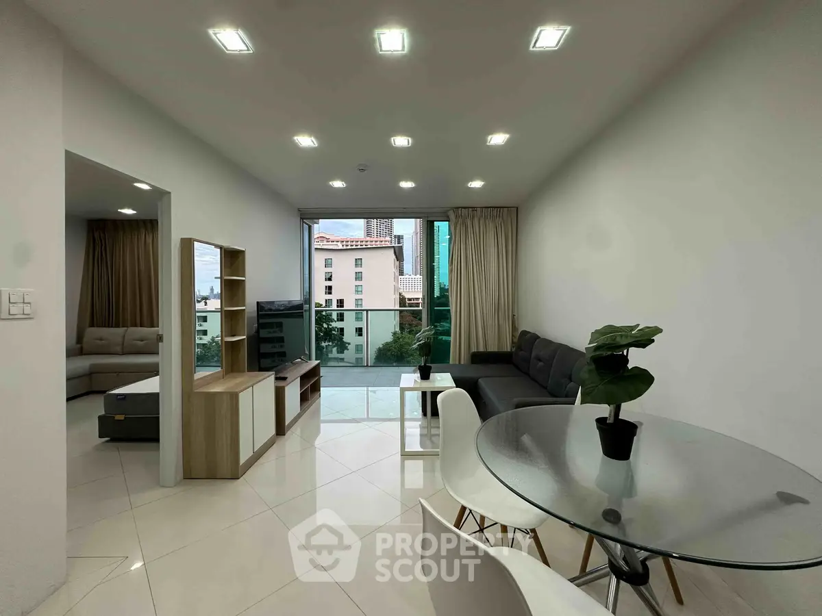 Modern living room with glass table, cozy sofa, and city view from balcony.