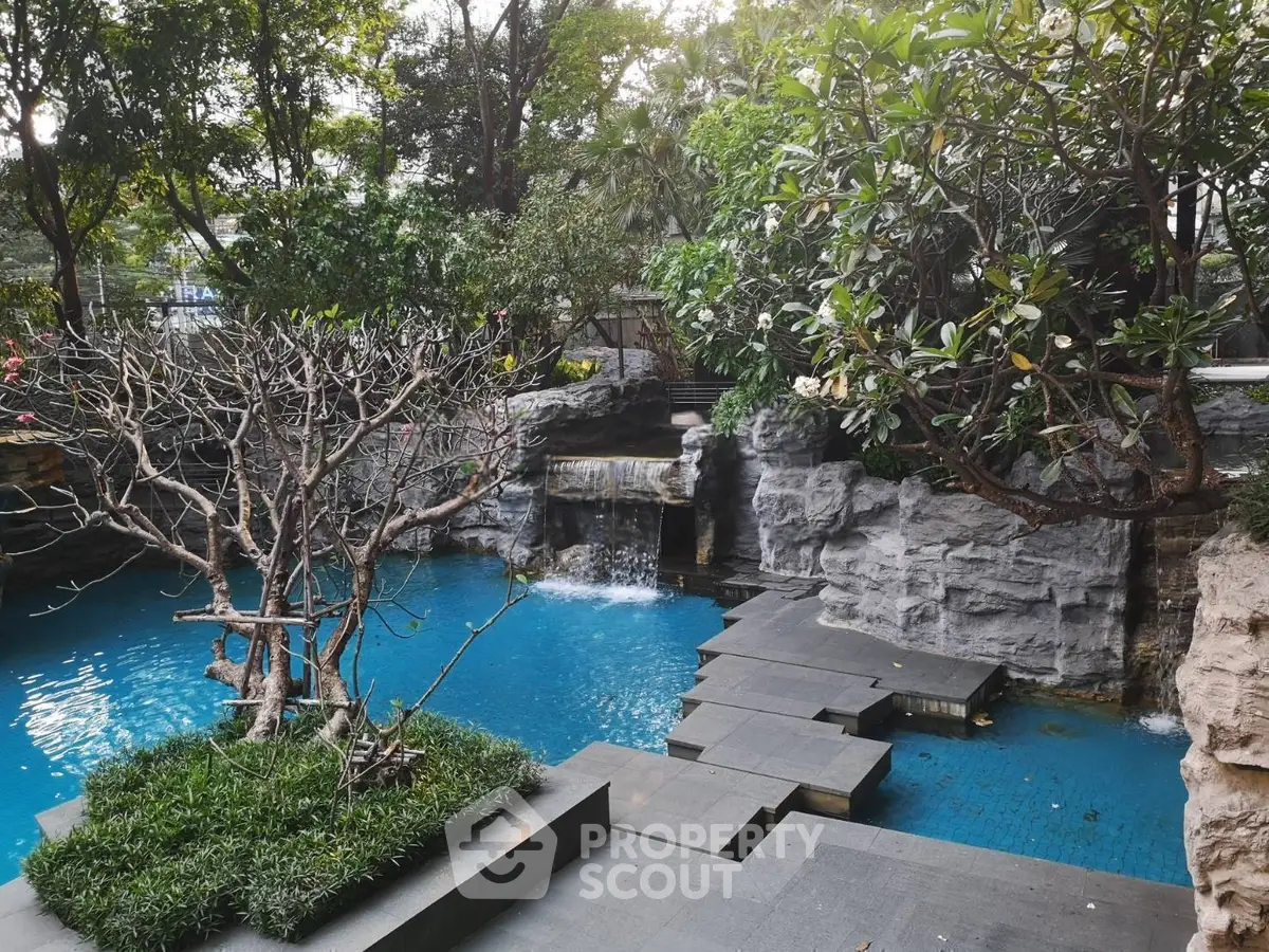 Luxurious outdoor pool with waterfall feature surrounded by lush greenery and stone pathways.