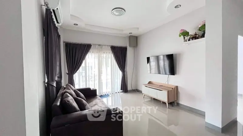 Spacious modern living room with glossy white tiles, elegant dark curtains, and sleek furniture, leading to a sunlit balcony.
