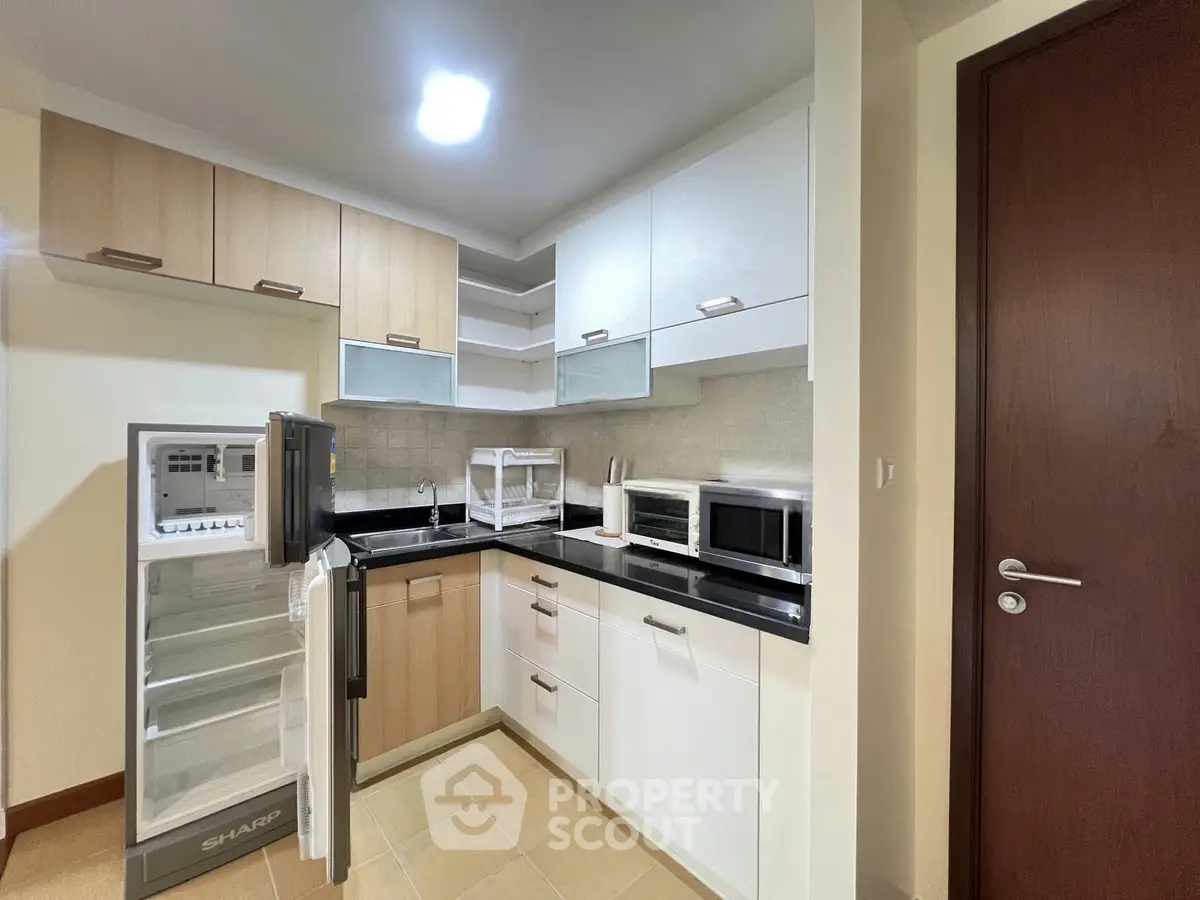 Modern kitchen with open fridge, microwave, and sleek cabinetry in a cozy apartment setting.
