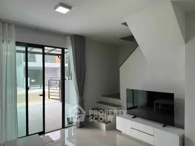 Modern living room with sleek staircase and large glass doors leading to outdoor area.