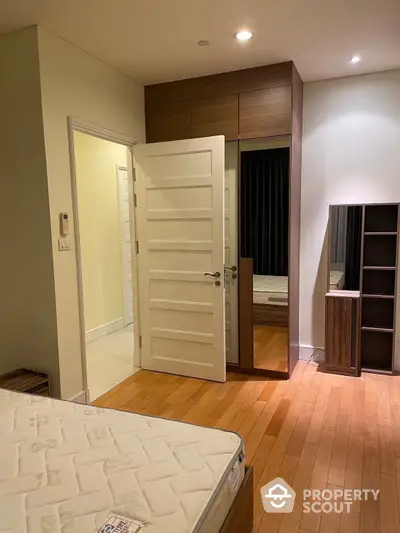 Cozy bedroom with warm wooden flooring, ample built-in storage, and modern lighting, perfect for urban living.