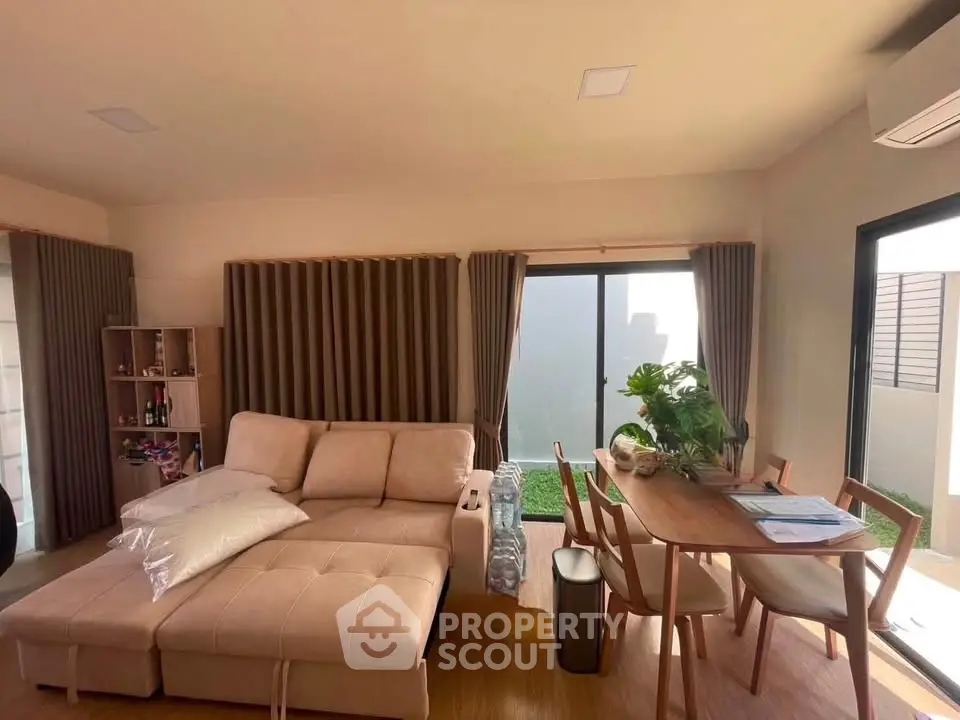 Modern living room with cozy sofa and dining area, featuring large windows and stylish decor.