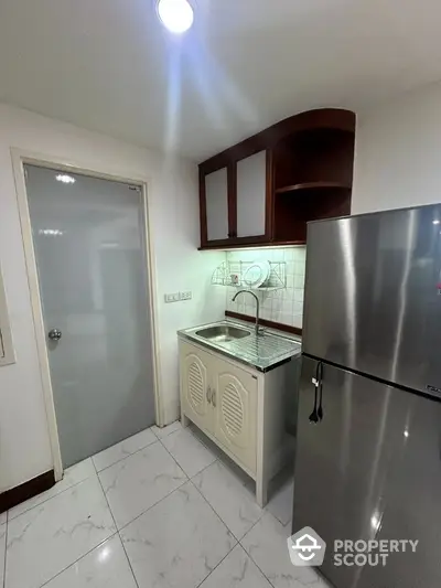 Compact kitchen with stainless steel fridge and modern cabinetry