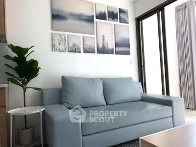 Modern living room with stylish blue sofa and nature-themed wall art, featuring large windows for natural light.