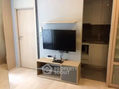 Modern apartment interior with sleek TV setup and compact kitchen area.