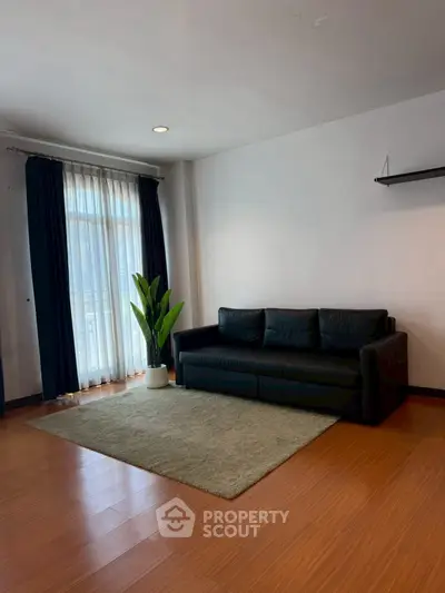 Spacious living room with modern black sofa and large window for natural light.
