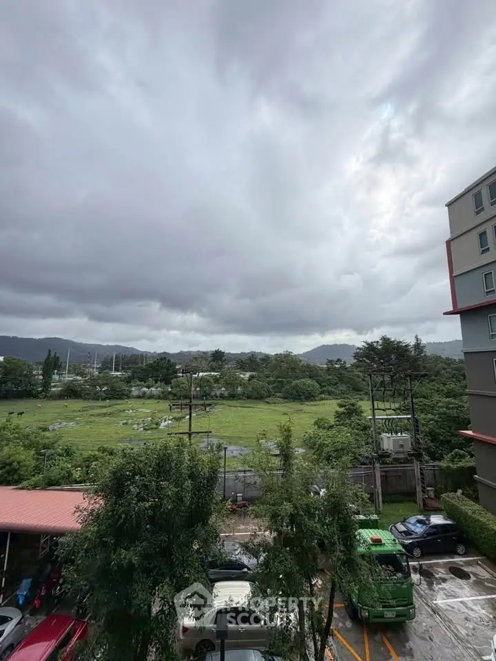 Scenic view from apartment balcony overlooking lush greenery and distant hills.