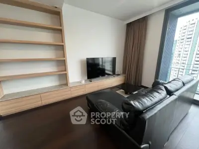 Modern living room with sleek black sofa and large TV, featuring floor-to-ceiling windows and built-in shelving.