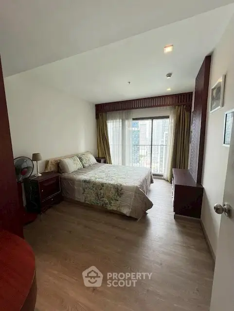 Cozy bedroom with city view and natural light, featuring elegant decor and wooden flooring.