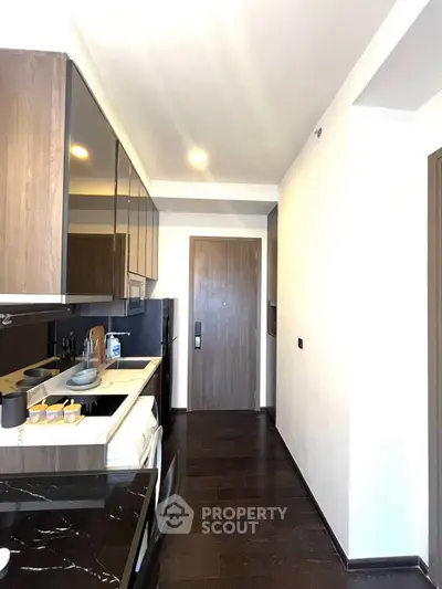 Modern kitchen with sleek dark wood cabinets and black countertops, featuring a closed layout and contemporary appliances.