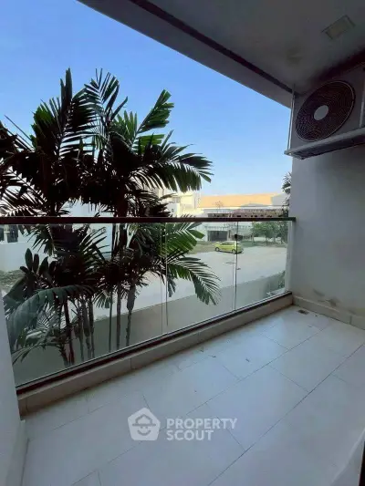 Spacious balcony with glass railing and lush greenery view, perfect for relaxation and outdoor enjoyment.