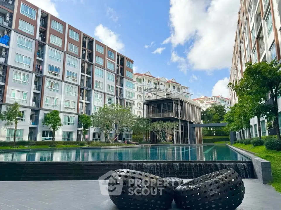 Modern apartment complex with pool and lush greenery under a clear blue sky.