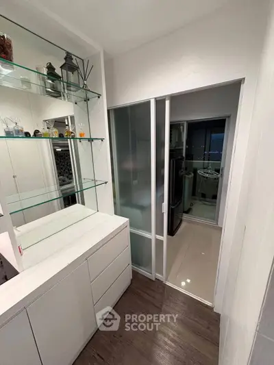 Modern kitchen with sleek white cabinetry and glass shelving, featuring a sliding glass door leading to a laundry area.