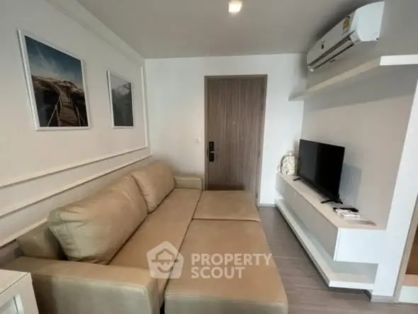 Modern living room with beige sofa, wall-mounted TV, and air conditioning unit.