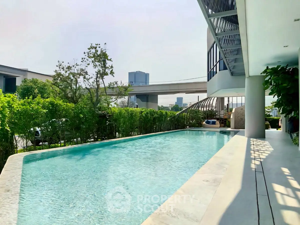 Luxurious modern poolside view with lush greenery and urban backdrop, perfect for relaxation and leisure.