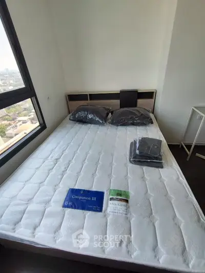 Cozy bedroom with large window offering city views, featuring a neatly made bed and modern decor.