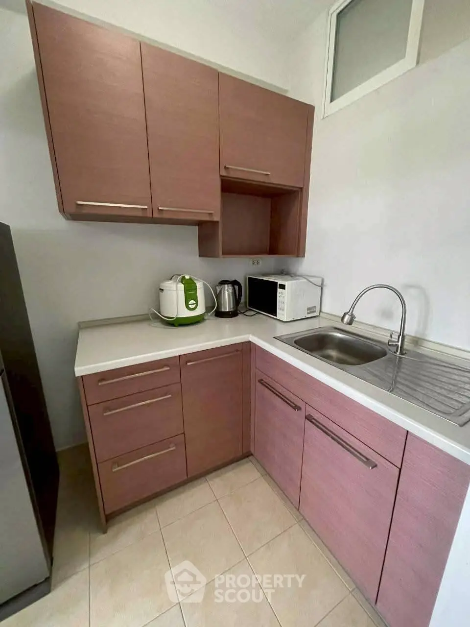 Modern kitchen with pink cabinets, stainless steel sink, and appliances like microwave and rice cooker.