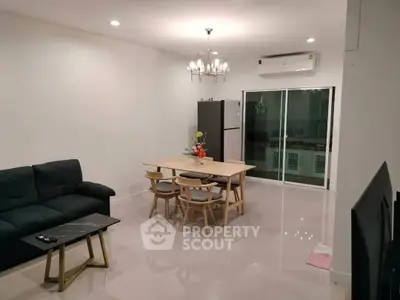 Modern living room with dining area and sleek furniture, featuring a chandelier and air conditioning.