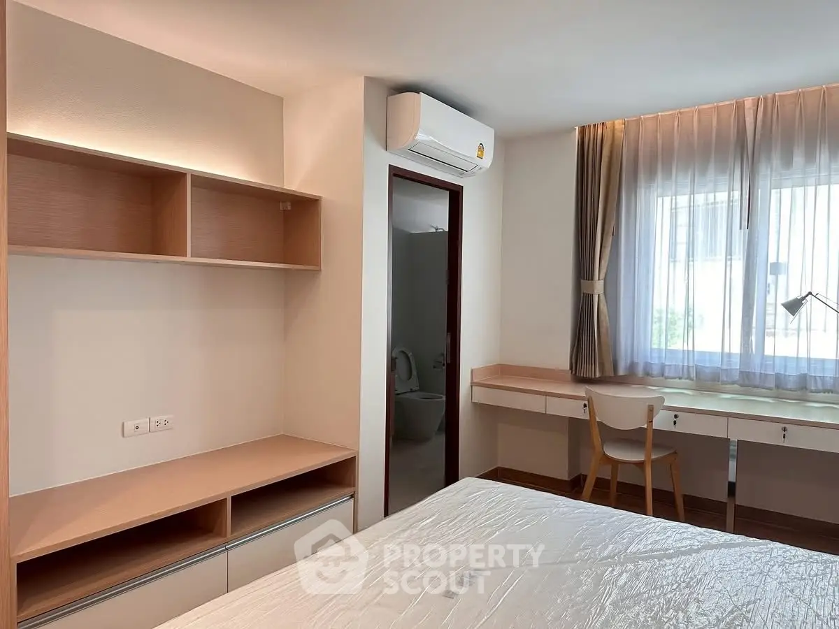 Modern bedroom with built-in shelves, desk, and air conditioning, featuring natural light from a large window.