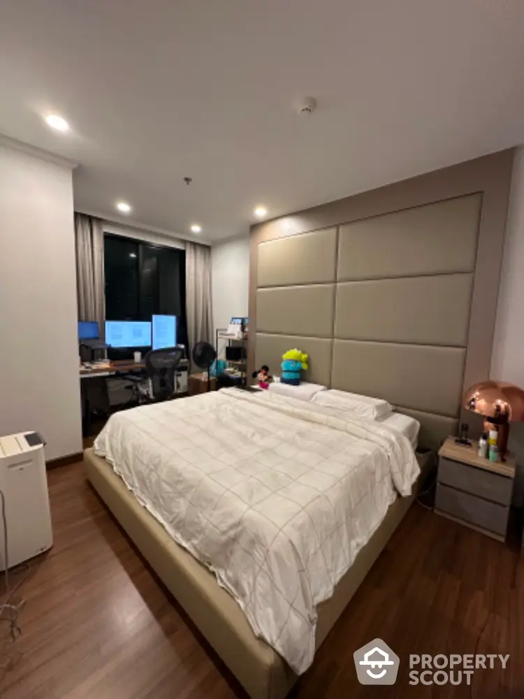 Spacious bedroom with large bed and modern home office setup, featuring elegant wood flooring and ambient lighting.