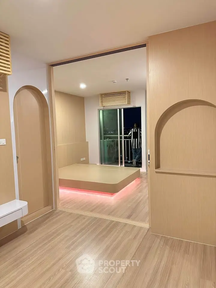 Modern interior with wooden flooring and sliding doors leading to a balcony with city view.